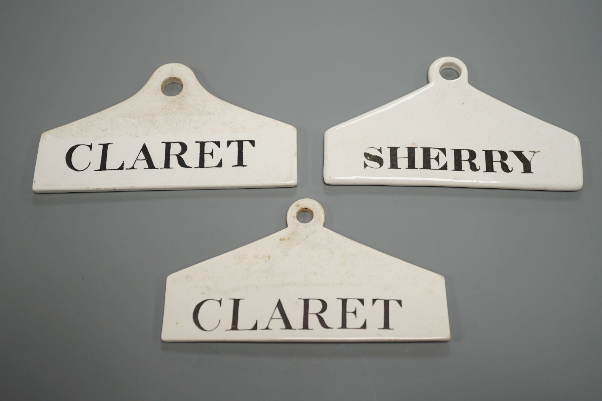 Three late 18th century creamware cellar labels, two claret stamped Wedgwood and one sherry, unmarked, 14 cms wide.